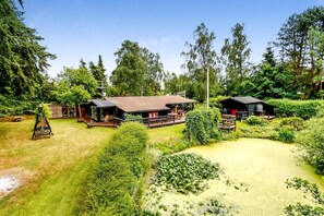 A lodge with a large deck, surrounded by dense forest and a pond. - Charming vacation home on large grounds (Rudkøbing)