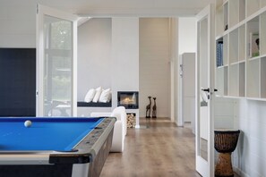 A modern living room with a pool table, a fireplace, and a bookshelf.