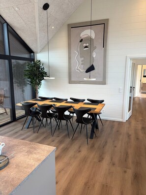 A modern dining area with a wooden table and black chairs, a large abstract painting on the wall, and a potted plant. - Lækkert sommerhus med udsigt over Limfjorden (Roslev)