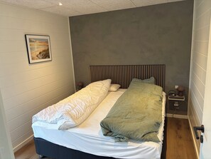A single bed with a headboard, a bedside table with a lamp, a power outlet, and a wall-mounted picture. - Lækkert sommerhus med udsigt over Limfjorden (Roslev)