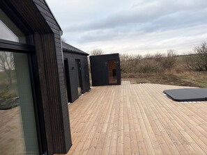 Un edificio moderno con una terraza de madera, un deslizador y un felpudo exterior negro.