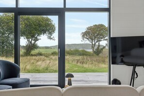 Ein Zimmer mit großem Fenster und Blick auf ein grünes Feld und Bäume.
