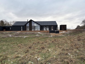 En modern svart byggnad med stora fönster, ett sluttande tak och en träveranda.