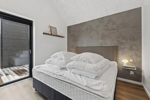 Un dormitorio con cama, mesita de noche, lámpara de pared y ventana con persianas.