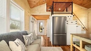 A cozy cabin interior with a sofa, wooden floors, a kitchen with a refrigerator, and a staircase. - Special Retreat in Nancy (Faubush)