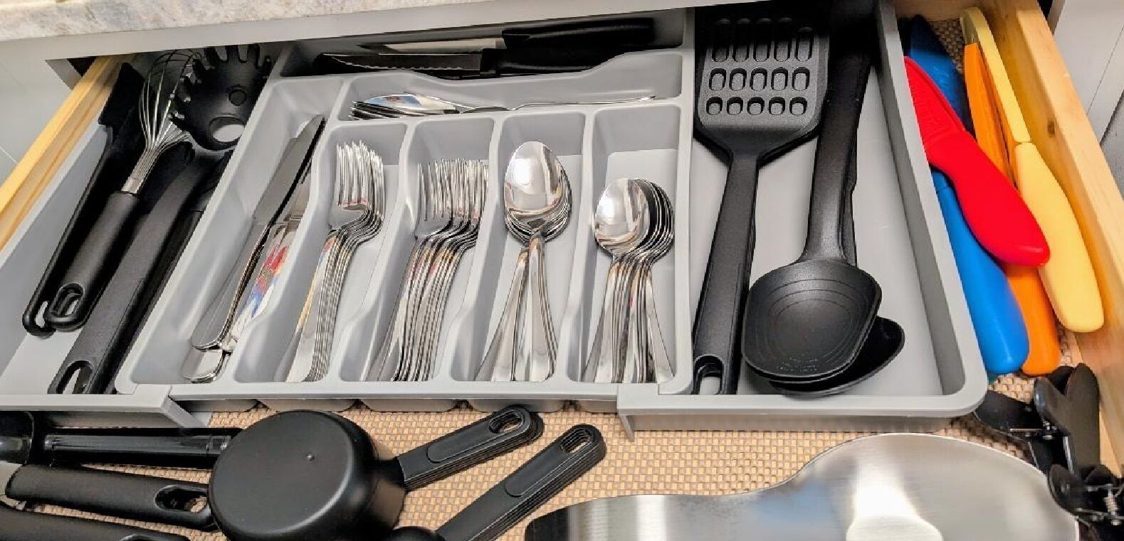 A drawer with neatly organized kitchen utensils including forks, spoons, spatulas, and tongs.
