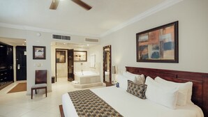 Een hotelkamer met een groot bed, een zithoek, een badkamer met bad en een plafondventilator.