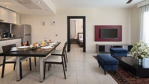 Een moderne woonkamer met een eethoek, een flatscreen televisie aan de muur en een zithoek met een blauwe bank en voetenbankje.