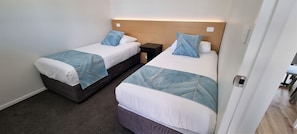 Habitación de hotel con dos camas, cada una con cabecero, mesitas de noche y piso alfombrado.