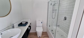Un baño moderno con lavamanos blanco, inodoro y zona de ducha con mampara de vidrio.
