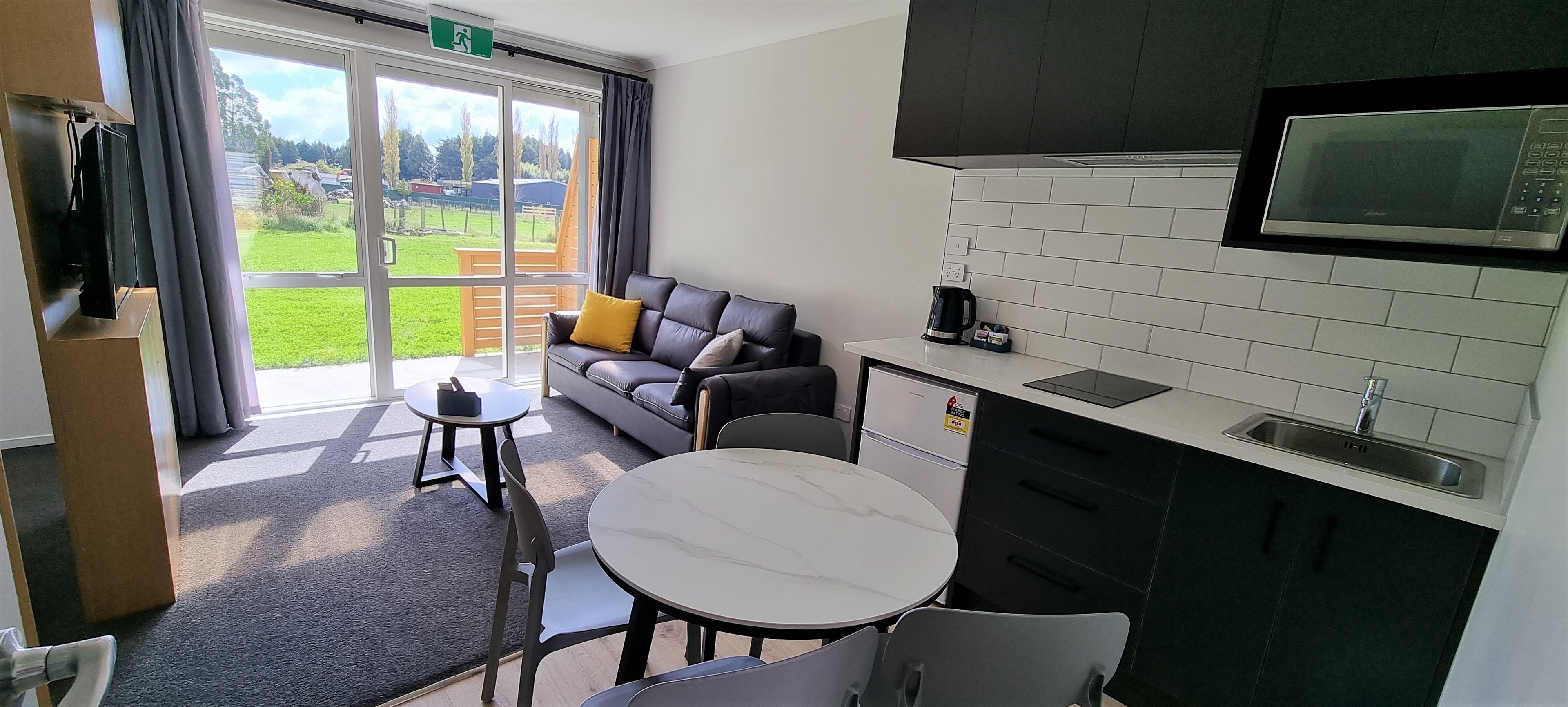 A modern kitchen with a microwave, sink, and cabinets. There is a dining area with a table and chairs, and a sofa with cushions.