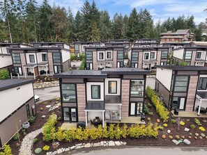 A modern residential complex with multiple two-story houses featuring large windows, outdoor seating areas, and well-maintained gardens. - Sunridge Beachside Retreat by EMR Vacation Rentals (Parksville)
