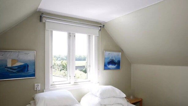 Un dormitorio con una cama, dos cuadros, una ventana y una mesita de noche.