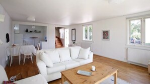 Un salón espacioso con un sofá blanco, una mesa de centro de madera y una zona de comedor con sillas y mesa blancos.