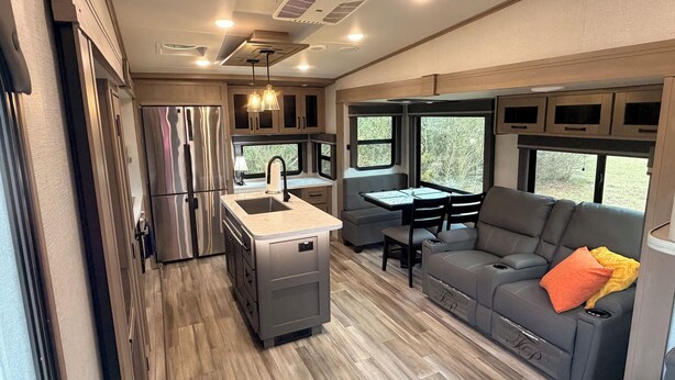 A compact RV kitchen with a stainless steel refrigerator, a sink, and a dining area with a table and chairs.