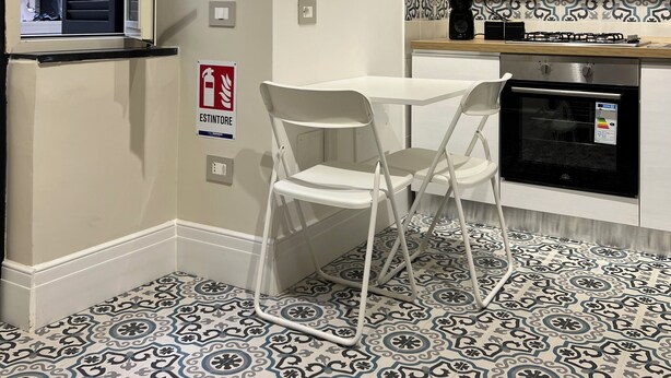 A compact kitchen with a window, a white table, two white chairs, a patterned backsplash, and a small oven. - Old town apartment, new and cozy (Napoli)