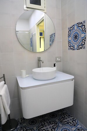 A bathroom with a round mirror, a white sink, and patterned floor tiles. - Old town apartment, new and cozy (Napoli)
