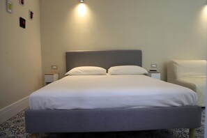 A neatly made bed with a grey headboard and white bedding in a room with a patterned floor. - Old town apartment, new and cozy (Napoli)