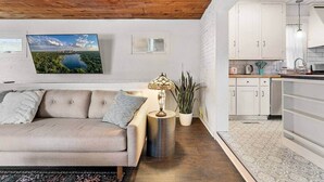 Uma sala de estar com sofá, luminária, planta e televisão na parede.