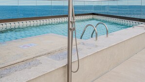 Ein Infinity-Pool auf dem Dach mit freiem Blick auf den Ozean, einer Duschbrause aus Metall und einer Holzbeschichtung.