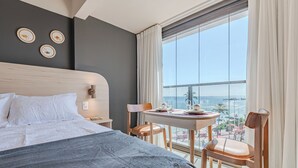 Ein Hotelzimmer mit Bett, Tisch mit Stühlen, Blick auf die Stadt und einem großen Fenster mit Vorhängen.