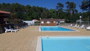 Zona de piscina con dos piscinas, rodeada de tumbonas y un edificio de madera con un letrero.