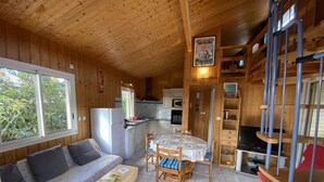 Interior acogedor de una cabaña con sofá, mesa de comedor, sillas, zona de cocina y escalera.