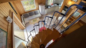 Interior de una cabaña de madera con comedor, cocina y una escalera.