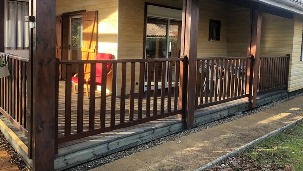Una cabaña de madera con un porche cubierto, una silla roja y un ventanal pequeño.