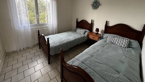 Een kamer met twee houten bedden, een raam met gordijnen, een radiator en een decoratie aan de muur.
