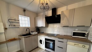 Een kleine keuken met een wasmachine, vaatwasser, magnetron en een raam met zonwering.