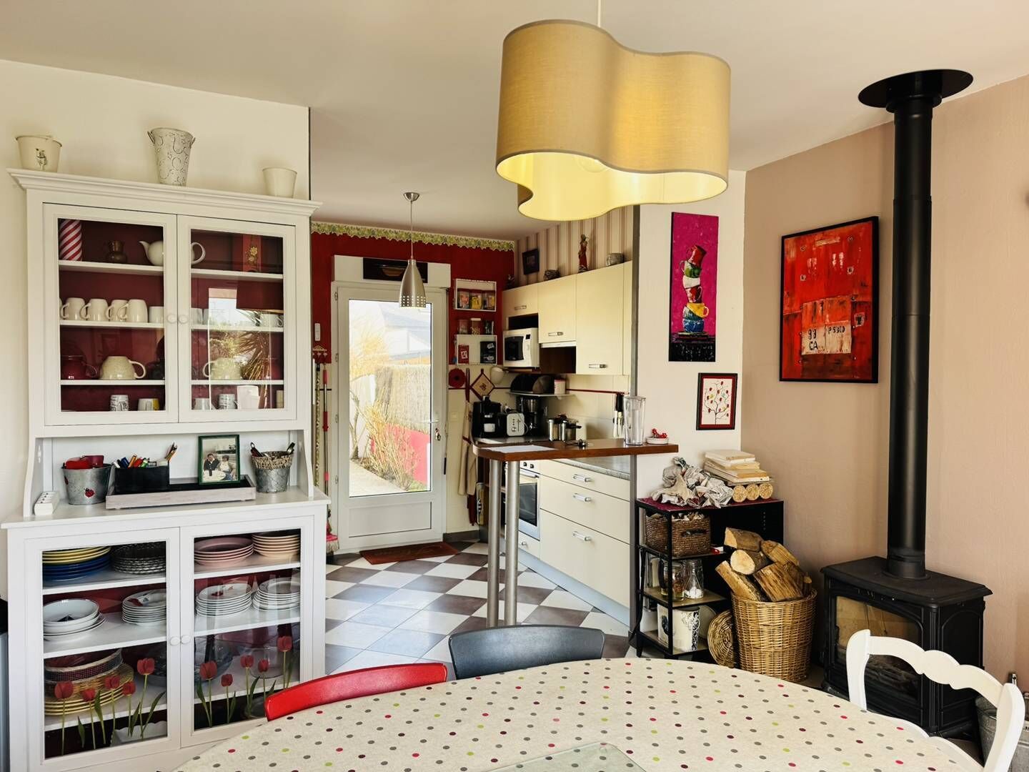 Een gezellige keuken met een eethoek, voorzien van een fornuis, kastjes en een eettafel met een tafelkleed met stippen.