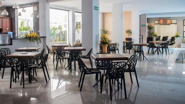A modern dining area with black chairs and tables, large windows, and a sign for 'Los Olivos'. - HOTEL PAIRUMANI (Cochabamba)