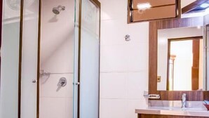 A bathroom with a glass-enclosed shower, a wooden vanity, and a mirror above the sink. - HOTEL PAIRUMANI (Cochabamba)