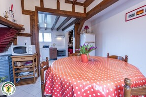 Une pièce chaleureuse avec une nappe à pois, des chaises en bois, une petite table en bois, un four à micro-ondes, un réfrigérateur et une plante en pot.
