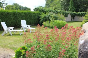 A garden with white lounge chairs, a hedge, and flowering plants. - Les Iris - OUTINES - Gîte (OUTINES)