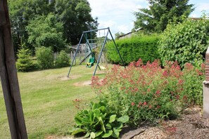 Un jardin avec une balançoire, une pelouse verdoyante et un parterre de fleurs roses.