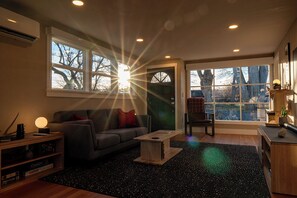 A modern living room with a sofa, coffee table, and a chair near large windows. - Restored 2BR Historic Cottage w/ Mesa Views – Grand Junction (Grand Junction)
