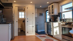 A modern kitchen with white cabinets, stainless steel appliances, and a view to the adjacent bathroom. - Restored 2BR Historic Cottage w/ Mesa Views – Grand Junction (Grand Junction)