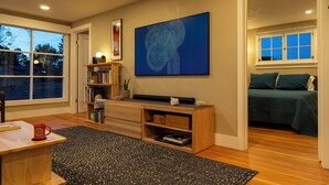 A modern living room with a large window, a bookshelf, a desk, and a bed. - Restored 2BR Historic Cottage w/ Mesa Views – Grand Junction (Grand Junction)