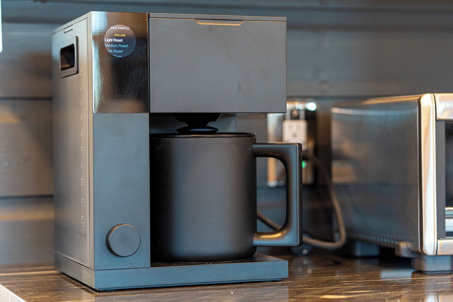 A coffee maker with a dark mug holder and a control panel with roast profiles.