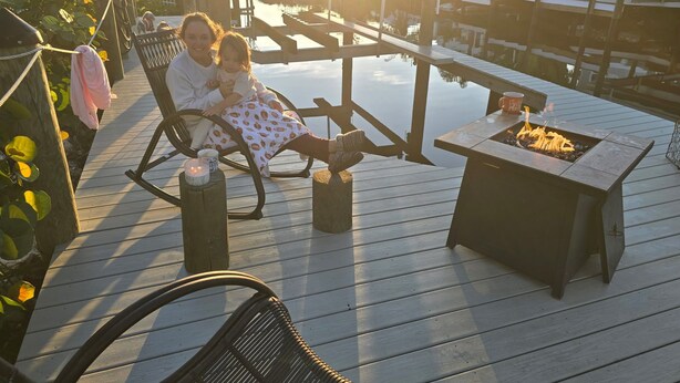 Ein Paar sitzt auf einer Holzterrasse mit einem Feuerkorb und Blick auf eine Marina.