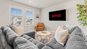 Een moderne woonkamer met grijze banken, een salontafel en een tv aan de muur met daarop 