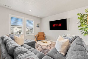 Een moderne woonkamer met grijze banken, een salontafel en een tv aan de muur met daarop 