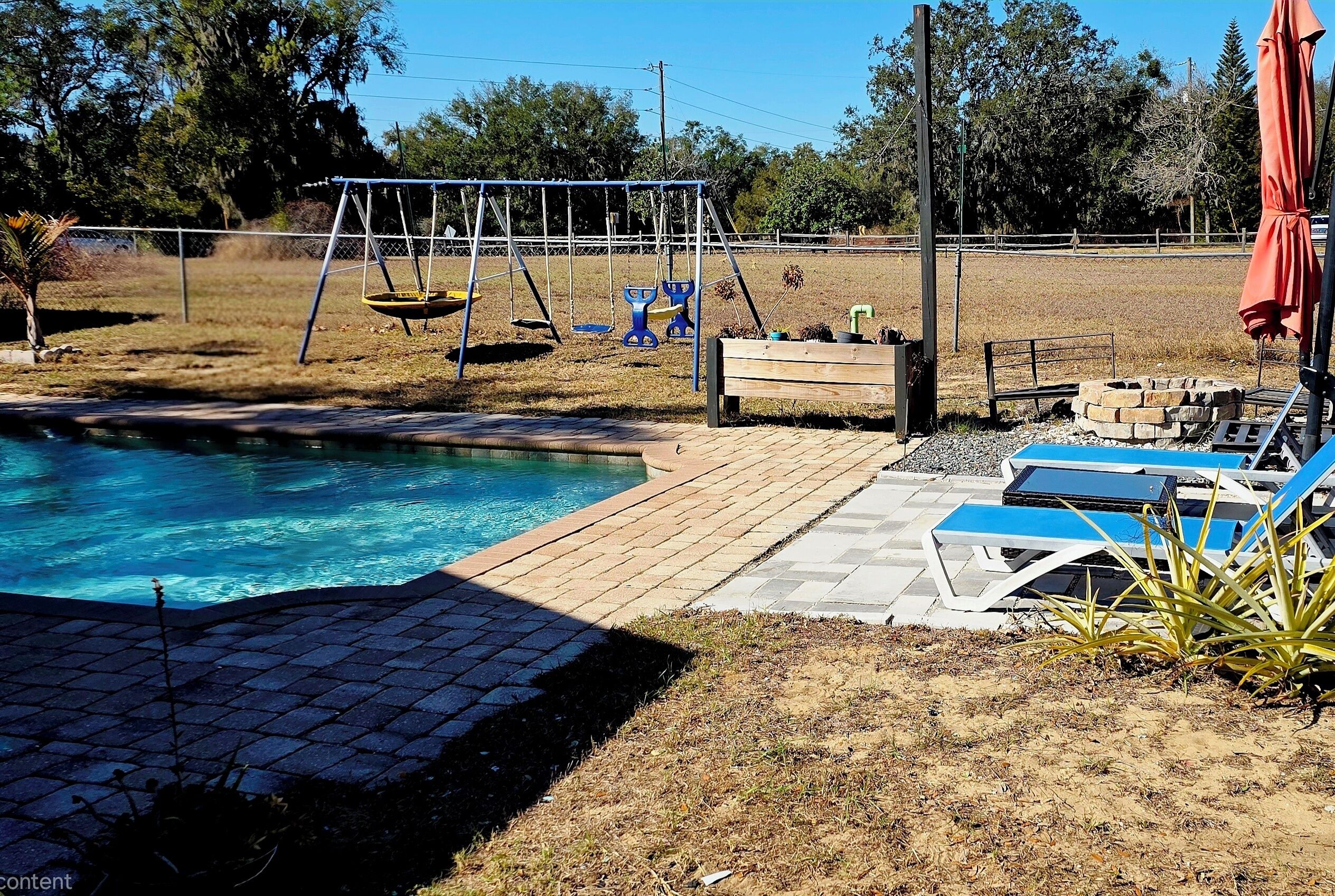 Un giardino con piscina, altalene e poltrone relax.