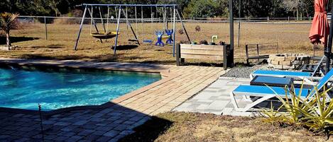 Un giardino con piscina, altalene e poltrone relax.