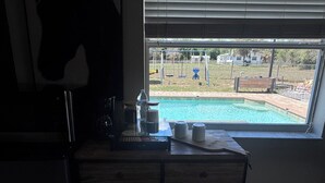 Una habitación con escritorio, ventana con vista a una piscina y una silla.