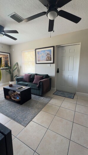 A living room with a ceiling fan, a couch, a coffee table, and a door. - Charming Private Suite Near Scenic Trails (Clermont)