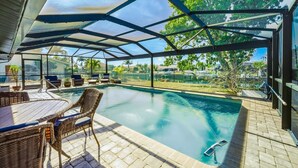 A covered outdoor swimming pool with a glass enclosure, wicker furniture, and a view of the surrounding landscape. - Punta Gorda Isles 3 Bedroom Pool Home on Canal (Punta Gorda)