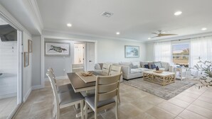 A spacious living area with a dining table, chairs, a sofa, and a coffee table. There is a ceiling fan, a window with curtains, and artwork on the walls. - Punta Gorda Isles 3 Bedroom Pool Home on Canal (Punta Gorda)